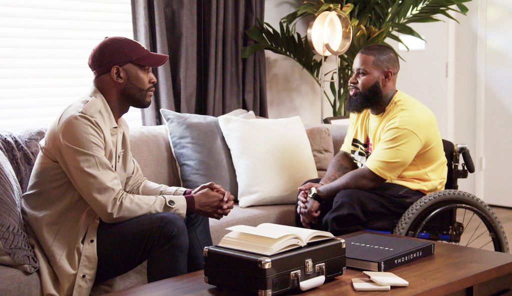 Karamo is sitting on a couch, Wesley is in his wheelchair opposite Karamo and they are talking