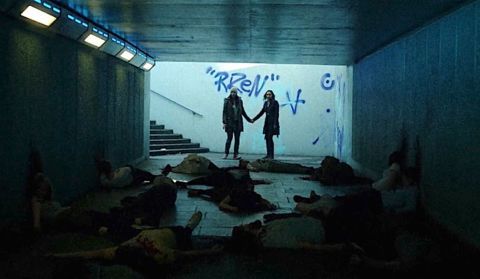 Still from the film Dawn of the Deaf. Two women are holding hands in a subway tunnel, and the floor is covered in bodies,